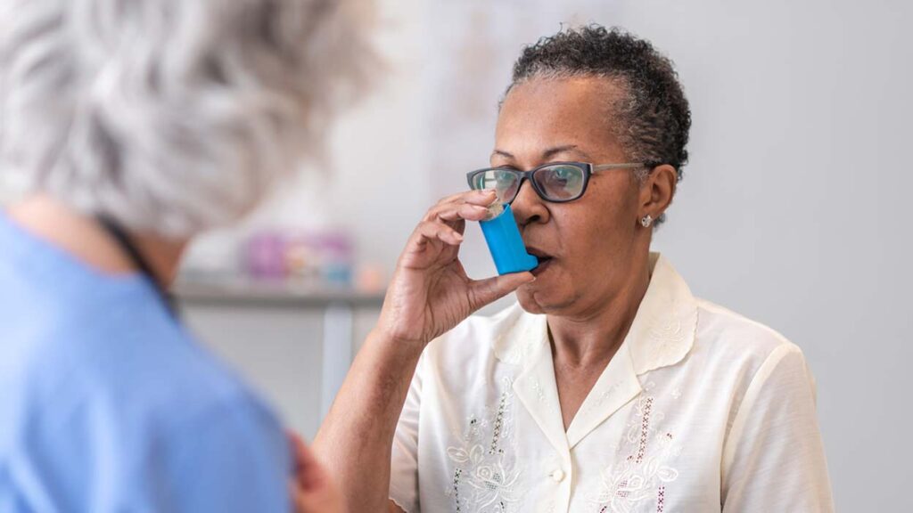A senior woman using an inhaler in front of her doctor